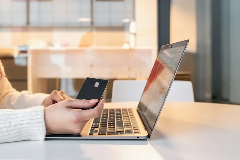 Hands holding a bank card next to an open laptop on a white table, shopping online